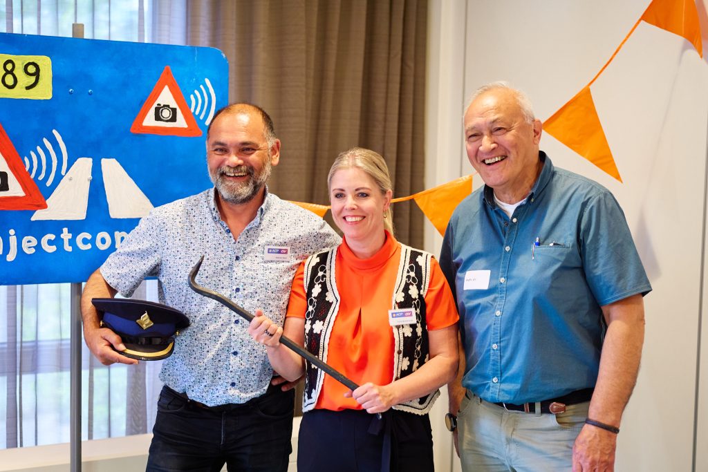 Three adults posing at a booth, smiling, with a blue banner and orange bunting in the background.