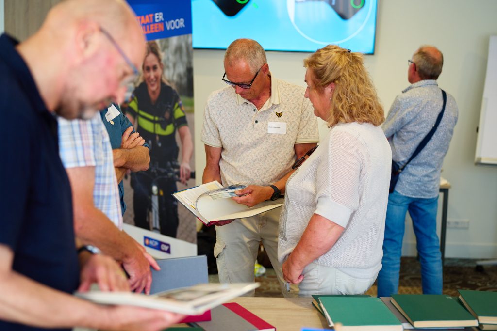Attendees at a conference booth examine brochures and papers, with name badges visible on their shirts.