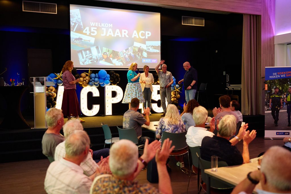 Audience on a stage applauds as presenters receive awards during an ACP 45-year celebration; large screen reads 'WELKOM 45 JAAR ACP'.