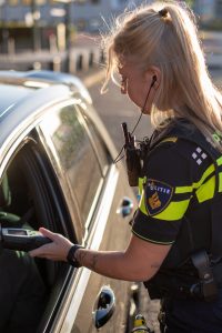 Police officer in a bright yellow jacket and police patch tests a driver using a handheld device at an open car window.