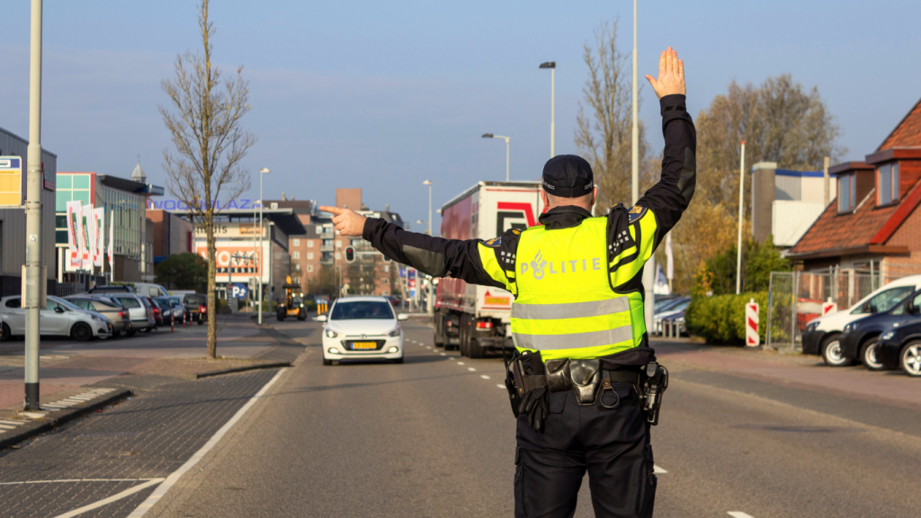 Policeman in a neon reflective vest directing traffic on a city street, with cars and a truck in view in the background