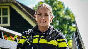Female firefighter in uniform with high-visibility stripes, radio and gear, outdoors near a building.